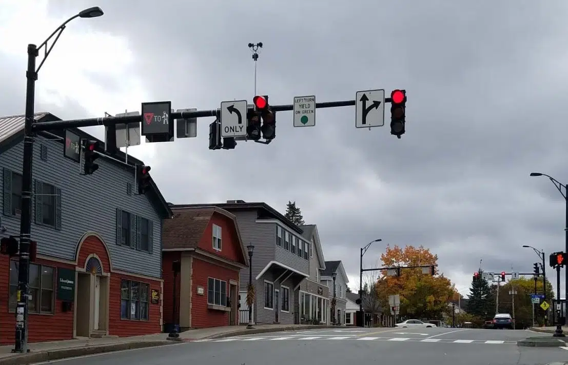 A quiet, small-town street showcases thoughtful traffic engineering, with red lights, buildings on the left, and autumn trees ahead under a cloudy sky.