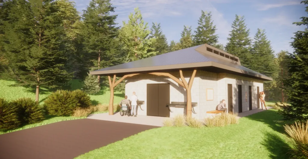 A small, modern building with a ramp, surrounded by grass and trees. Two people stand near the entrance, one in a wheelchair, and another sits on a bench outside.