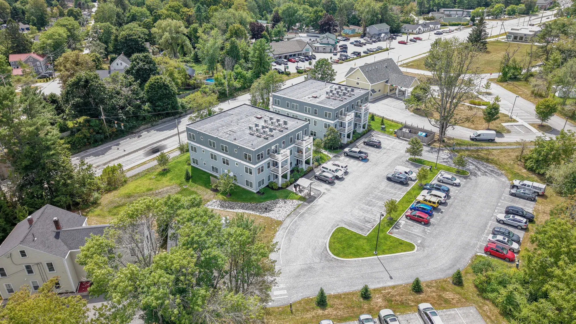 default - Sebago Technics Aerial view of two light-gray apartment buildings with a parking lot, showcasing civil engineering services in a tree-lined suburban area near local roads.