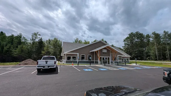 A modern, single-story building with large windows, designed through expert civil engineering services, sits by a parking lot with accessible spots, surrounded by trees under a cloudy sky.