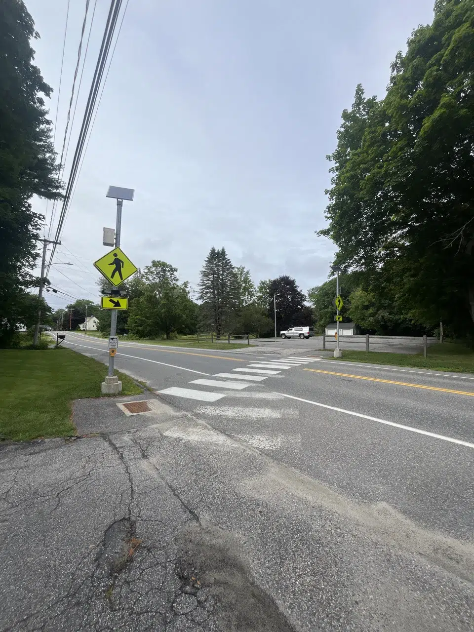 WINDHAM ACTIVE TRANSPORTATION PLAN 3 - Sebago Technics A crosswalk on a quiet street with pedestrian crossing signs, surrounded by trees and grassy areas under a cloudy sky.