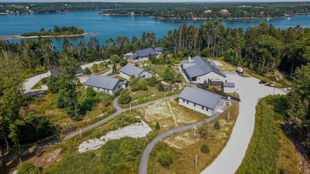 Aerial view of several houses surrounded by trees near a large blue lake, showcasing landscape architecture in Maine with winding roads connecting the properties.